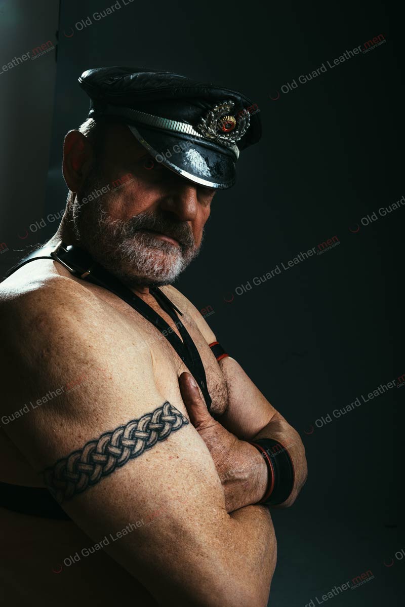 mature leather bear wearing a muir cap and having tatted arms